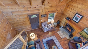 Ein Interieur einer Holzhütte mit Treppe, einer Couch, einem Kamin und einem gerahmten Bild an der Wand.