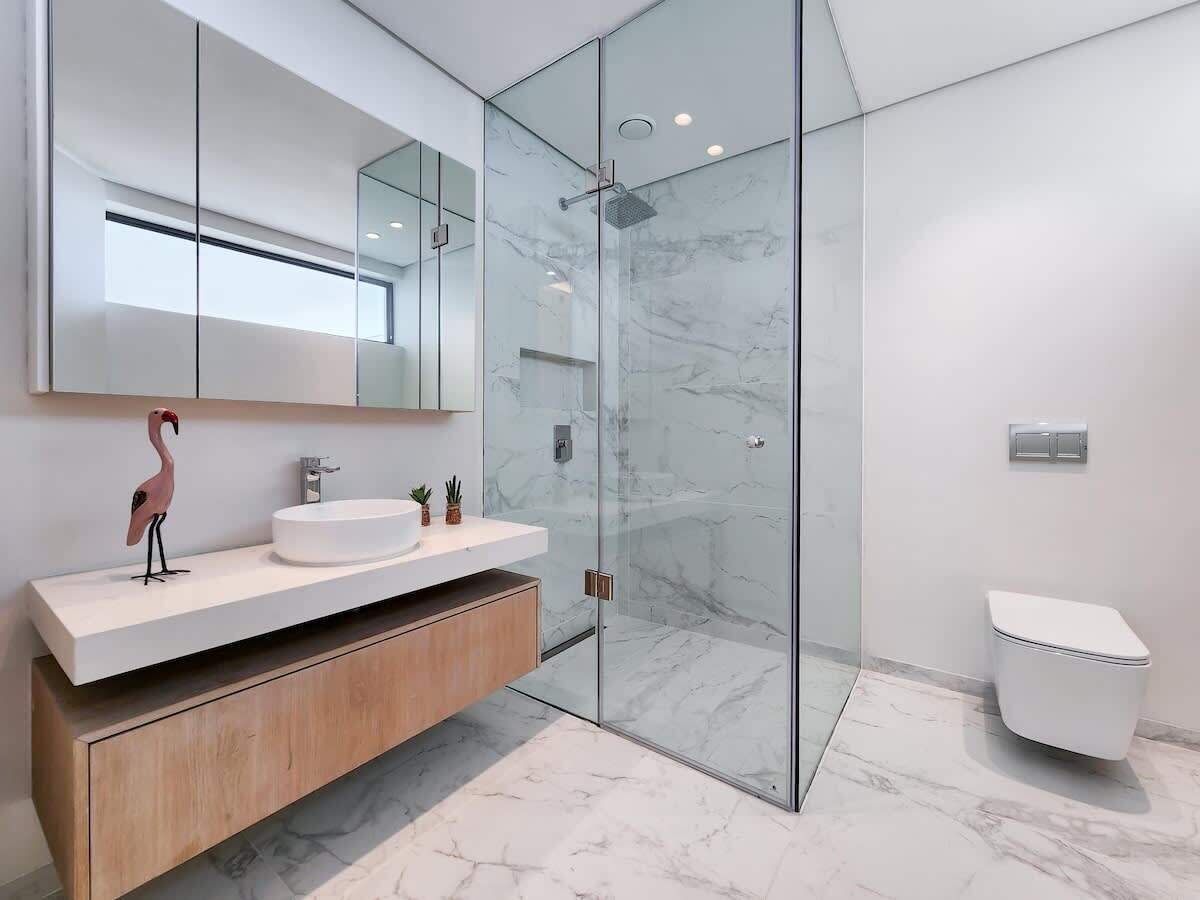 A modern bathroom with a glass-enclosed shower, a white sink, and a toilet.