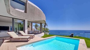 Une maison moderne dotée d’une piscine, de chaises longues et offrant une vue sur l’océan.
