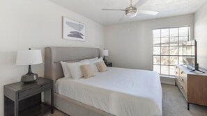 Een moderne slaapkamer met een bed, nachtkastjes, een bureau en een plafondventilator.