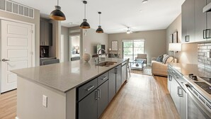 A modern kitchen with a large island, dark cabinetry, and pendant lighting. - Landing | Modern 1BD, Clubhouse, Yoga Studio (Phoenix)