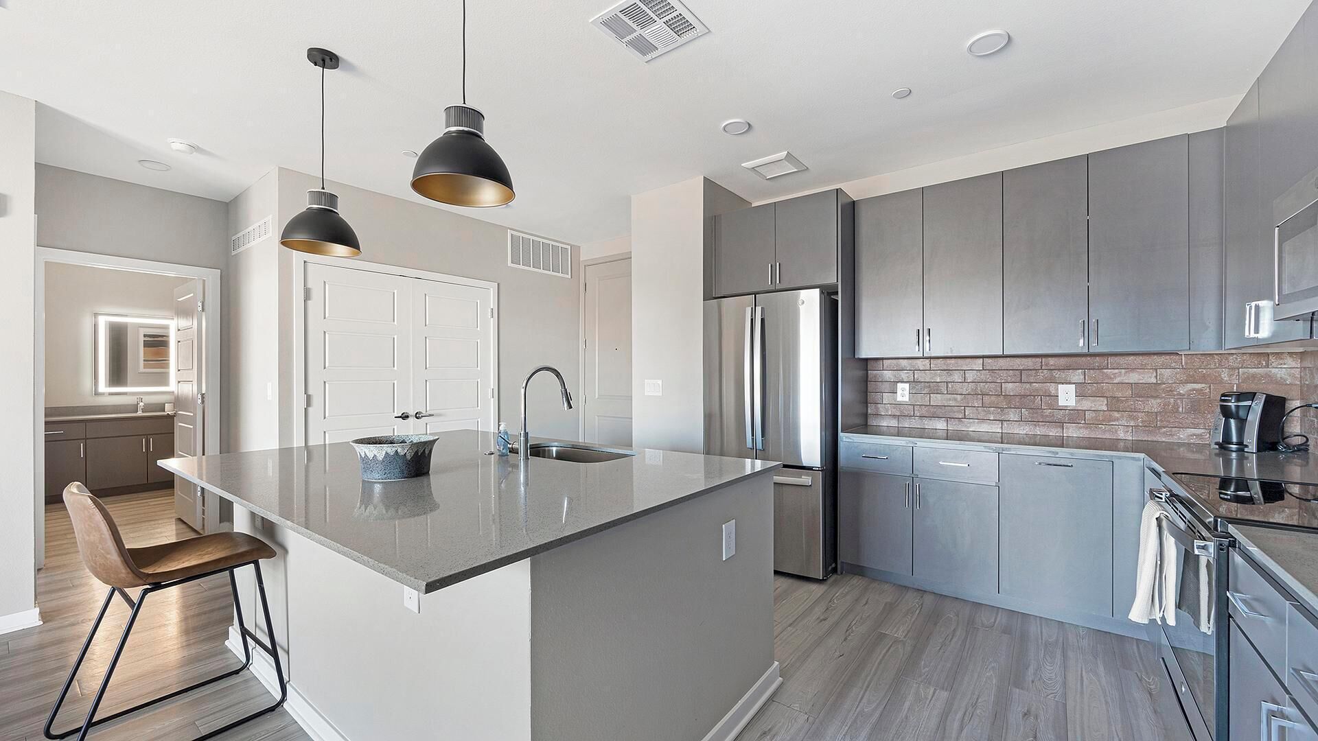 A modern kitchen with grey cabinets, a stainless steel refrigerator, and a large island with a sink.