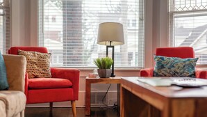 Un salón acogedor con un sillón rojo, una mesa de centro de madera con una lámpara, y vistas amplias por grandes ventanales.