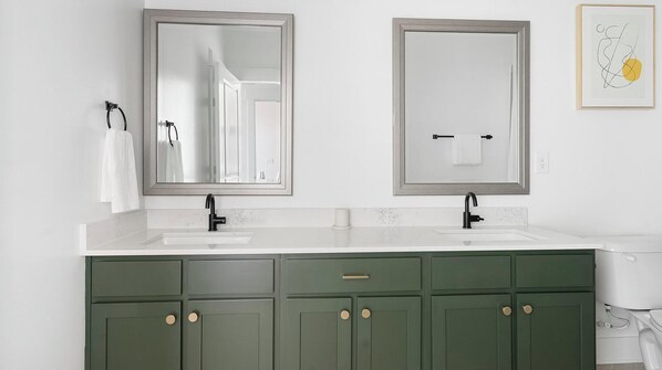 Une salle de bain avec deux lavabos, des meubles verts et une œuvre d’art encadrée au mur.