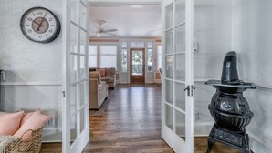 A hallway with a wooden floor, a black stove, a clock, and a door leading to a living room with a sofa. - 1913 Restored Lux Retreat|Walk2Dwtn/Ferry/5 bathrm (Bradenton)