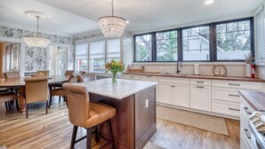 A spacious kitchen with a large island, white cabinetry, and a view of the outdoors through large windows. - 1913 Restored Lux Retreat|Walk2Dwtn/Ferry/5 bathrm (Bradenton)