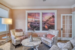 Ein Wohnzimmer mit zwei gemusterten Sesseln, einem runden Couchtisch und einem großen Fenster mit Sonnenuntergangsblick.
