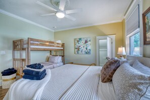 A bedroom with bunk beds, a bed with pillows, a ceiling fan, a painting, a lamp, and a window. - DOWNTOWN BRADENTON RETREAT | SWIM SPA • AMI • IMG (Bradenton)