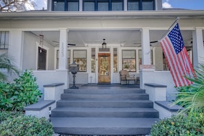 A two-story building with a porch, steps leading to the entrance, a flag, and a sign indicating the property is for sale. - DOWNTOWN BRADENTON RETREAT | SWIM SPA • AMI • IMG (Bradenton)