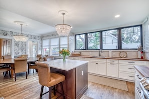 A spacious kitchen with a large island, wooden flooring, and a view through the windows. - DOWNTOWN BRADENTON RETREAT | SWIM SPA • AMI • IMG (Bradenton)