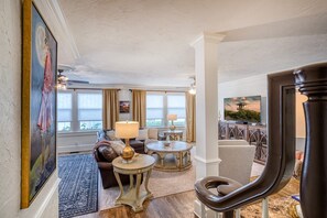 A spacious living room with a large window, a sofa, a coffee table, and a television. - DOWNTOWN BRADENTON RETREAT | SWIM SPA • AMI • IMG (Bradenton)