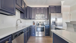 A modern kitchen with dark cabinetry, stainless steel appliances, and a dishwasher. - Landing | Modern 1BD, Pool, Courtyard (Cary)