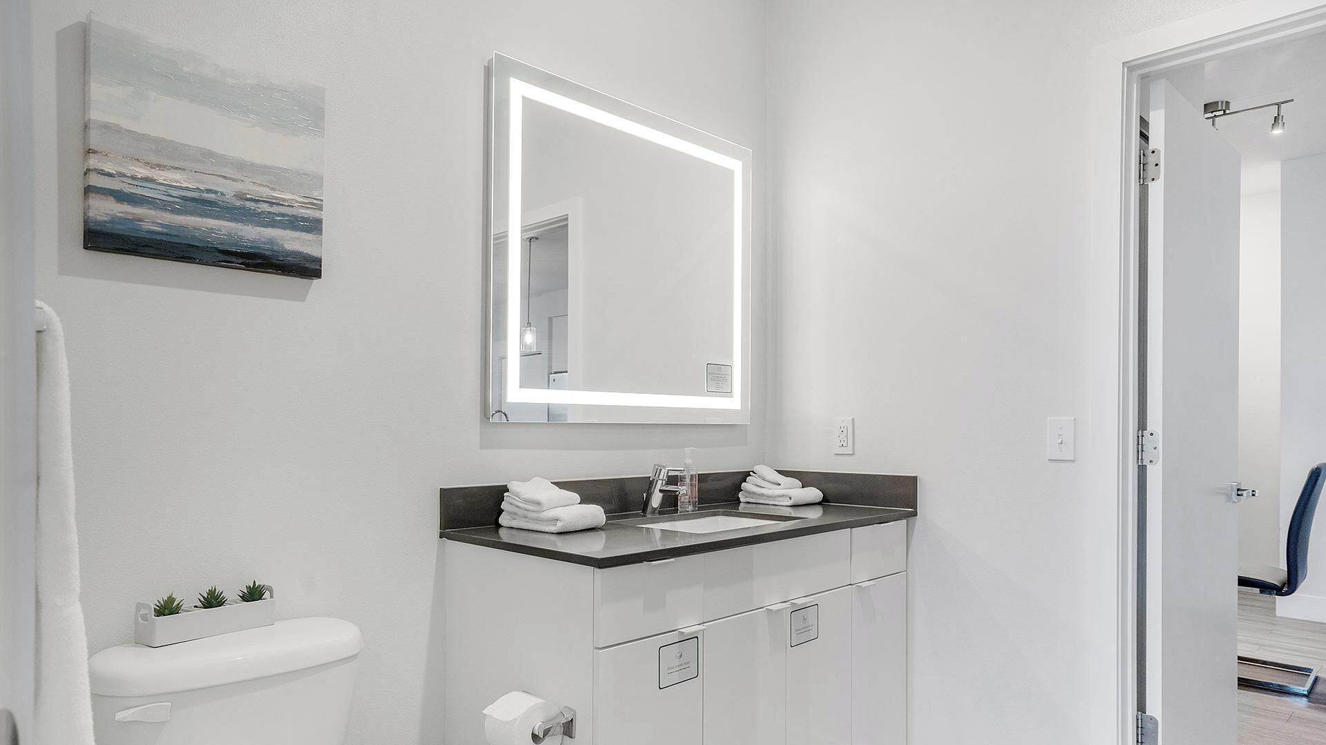 A modern bathroom with a white toilet, a sink with a mirror above it, and a towel rack.