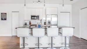 A modern kitchen with white cabinetry, stainless steel appliances, and a central island with bar stools. - Landing | Beautiful 2BD, Gym, Pool (Tampa)