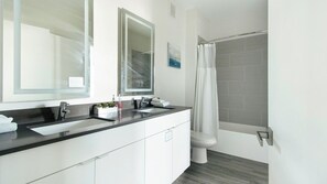 Ein modernes Badezimmer mit einem Doppelwaschtisch, einem großen Spiegel und einer Dusche mit Glastür.