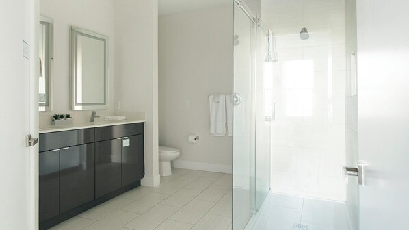 A modern bathroom with a dark grey vanity, a white toilet, and a glass shower enclosure. - Landing | Chic 3BD, Pool, Clubhouse (Tampa)