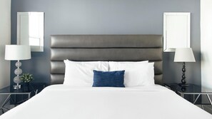 Ein ordentlich bezogenes Bett mit weißen und blauen Kissen, einem dunklen Kopfteil sowie zwei Nachttischen mit Lampen und Dekoration.