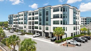 A multi-story residential building with a modern design, featuring a parking lot with several cars and palm trees. - Landing | Incredible 3BD, Gym, Clubhouse (Tampa)