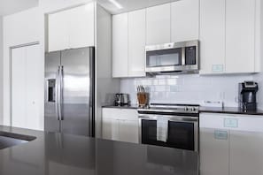 A modern kitchen with stainless steel appliances, white cabinetry, and a black countertop. - Landing | Spectacular 2BD, Gym, Clubhouse (Tampa)