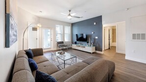 A modern living room with a sectional sofa, a glass coffee table, and a flat-screen TV mounted on a dark accent wall. - Landing | Stylish 3BD, Clubhouse, Gym (Tampa)