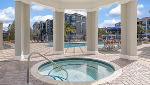 A pool area with a hot tub, lounge chairs, and a view of apartment buildings.