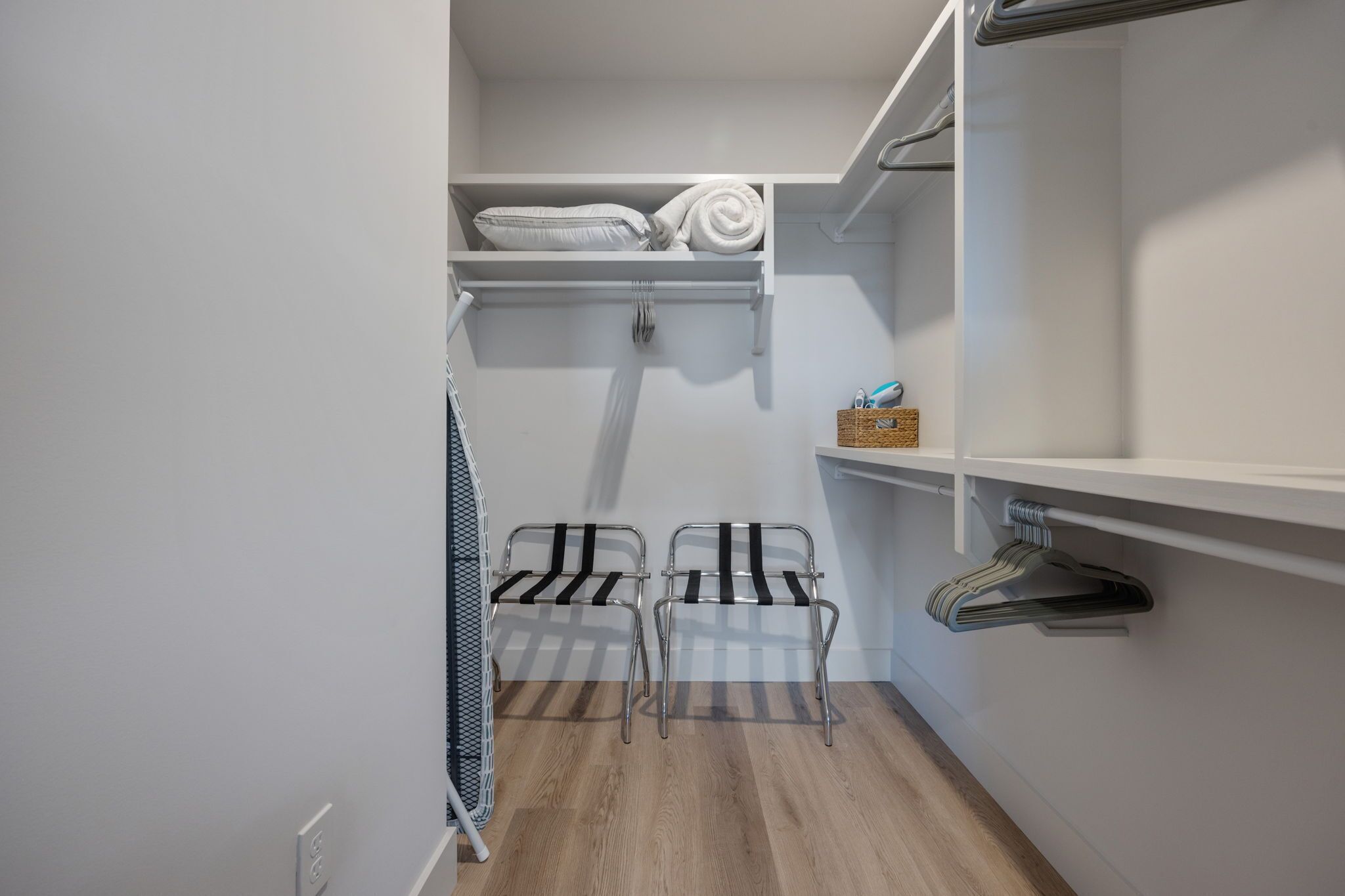 A walk-in closet with shelves for folded towels, a hanging rack for clothes, and a metal chair.