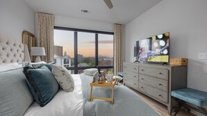 Una habitación de hotel moderna con una cama grande, televisor, cómoda y vistas a la ciudad.