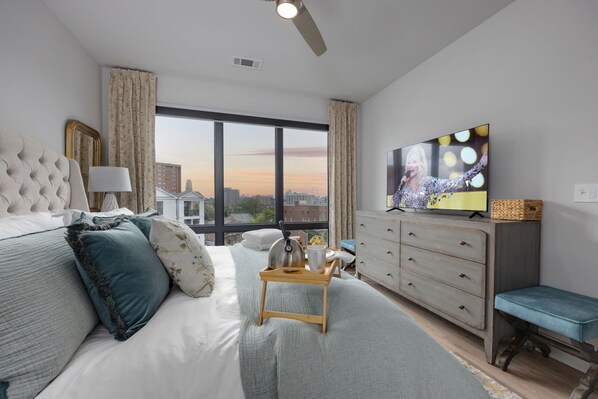 Una habitación de hotel moderna con una cama grande, televisor, cómoda y vistas a la ciudad.