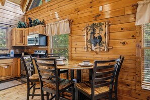 A wooden cabin interior with a dining table, chairs, a microwave, and a bear-themed wall decoration. - Stunning Views, Games, and Relaxation! (GATLINBURG)