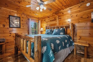 A wooden cabin bedroom with a bed, a ceiling fan, and a window.