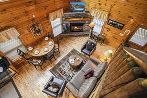 A cozy cabin interior with a fireplace, wooden walls, a dining area, and a seating space.