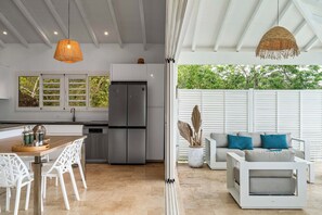A modern kitchen with a built-in refrigerator, white cabinetry, and a dining area with white chairs. - Villa La Sucrerie - Three Bedroom Villa, Sleeps 6 (Les Anses-d'Arlet)