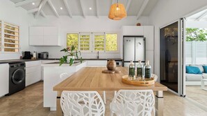 Una cocina moderna con una isla central, muebles blancos y un ventanal con vista a follaje.