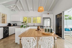 A modern kitchen with a central island, white cabinetry, and a large window with a view of greenery. - Villa La Sucrerie - Three Bedroom Villa, Sleeps 6 (Les Anses-d'Arlet)