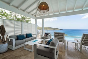 A covered outdoor seating area with a view of the sea, white furniture, and a hanging light fixture. - Villa La Sucrerie - Three Bedroom Villa, Sleeps 6 (Les Anses-d'Arlet)