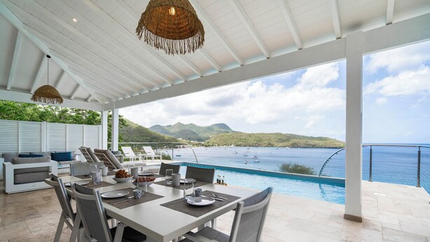 Un espacio de comedor al aire libre cubierto, con piscina y vista al mar.