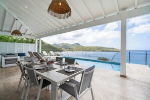 Un espace extérieur abrité, aménagé pour les repas, avec une piscine et une vue sur la mer.