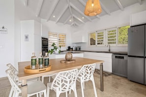 A modern kitchen with white cabinetry, a wooden dining table, and a stainless steel refrigerator. - Villa La Sucrerie - Three Bedroom Villa, Sleeps 6 (Les Anses-d'Arlet)
