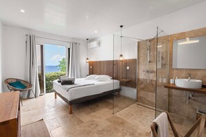 A modern bedroom with a bed, a glass shower enclosure, a wooden bedside table, and a view of the sea. - Villa La Sucrerie - Three Bedroom Villa, Sleeps 6 (Les Anses-d'Arlet)
