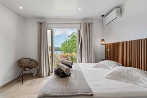 A bedroom with a bed, a chair, a view of the outdoors, and an air conditioning unit. - Villa La Sucrerie - Three Bedroom Villa, Sleeps 6 (Les Anses-d'Arlet)