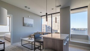 A modern apartment with a kitchenette, a dining area, a sofa, and a large window offering a city view. - Landing | Amazing 2BD in Fountain Heights (Birmingham)