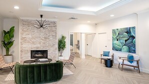 A modern living room with a fireplace, a green sofa, a coffee table, and a large abstract painting on the wall. - Landing | Chic Studio, Gym, Pool (Raleigh)