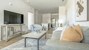 A modern living room with a flat-screen TV, a grey sofa, a coffee table, and a kitchen in the background. - Landing | Incredible 1BD, Clubhouse, Gym (Charlotte)
