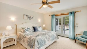 Un dormitorio con cama, mesitas de noche, ventilador de techo, ventana con cortinas y vistas al exterior.