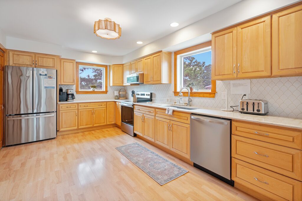 A modern kitchen with wooden cabinets, stainless steel appliances, and a large window.