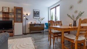 Un salon avec un téléviseur, des meubles en bois, une table à manger avec des chaises, un fauteuil bleu, un buffet en bois, un tableau encadré et une lampe sur pied.