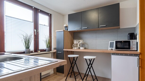 Une cuisine moderne dotée d’un plan de travail en bois, de deux tabourets de bar, d’un four à micro-ondes, d’une machine à café et d’un réfrigérateur.