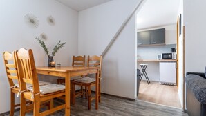 Un espace de vie compact comprenant une table et des chaises de salle à manger en bois, un petit coin cuisine équipé d’appareils électroménagers et un coin salon confortable.