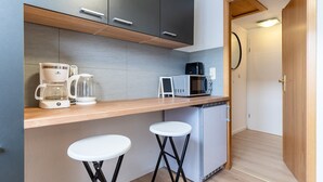Une cuisine compacte équipée d’une machine à café, d’un four à micro-ondes et d’un petit réfrigérateur. On y trouve deux tabourets et un plan de travail en bois.
