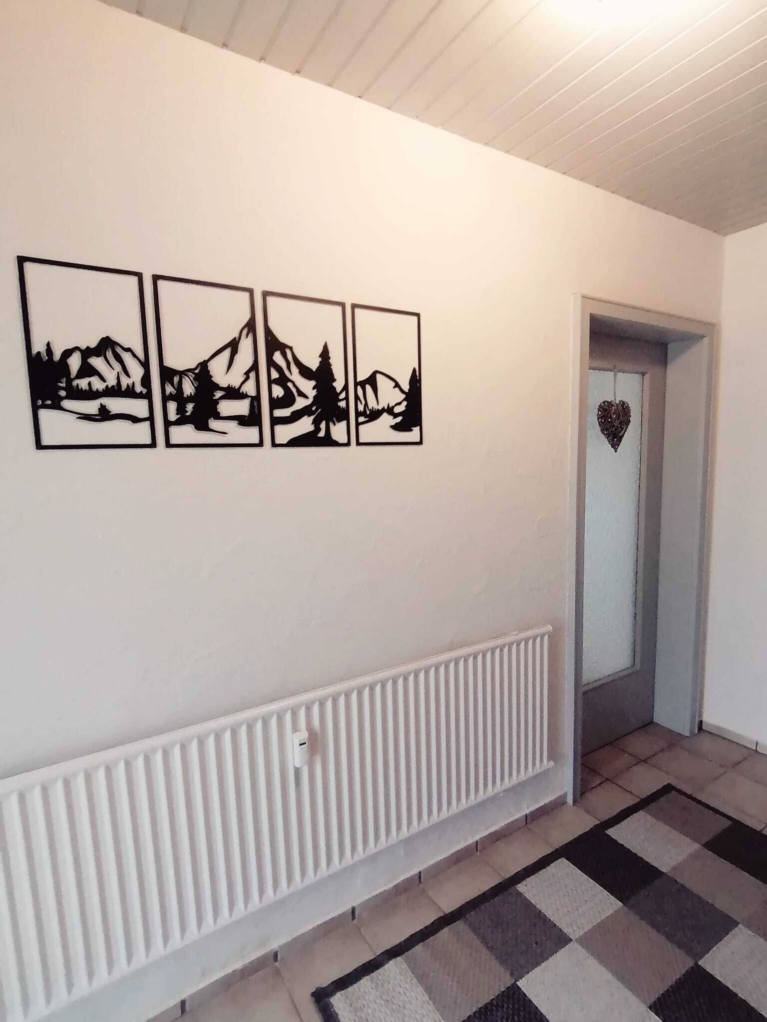 A hallway with a radiator, a checkered rug, and four black and white mountain landscape pictures on the wall.